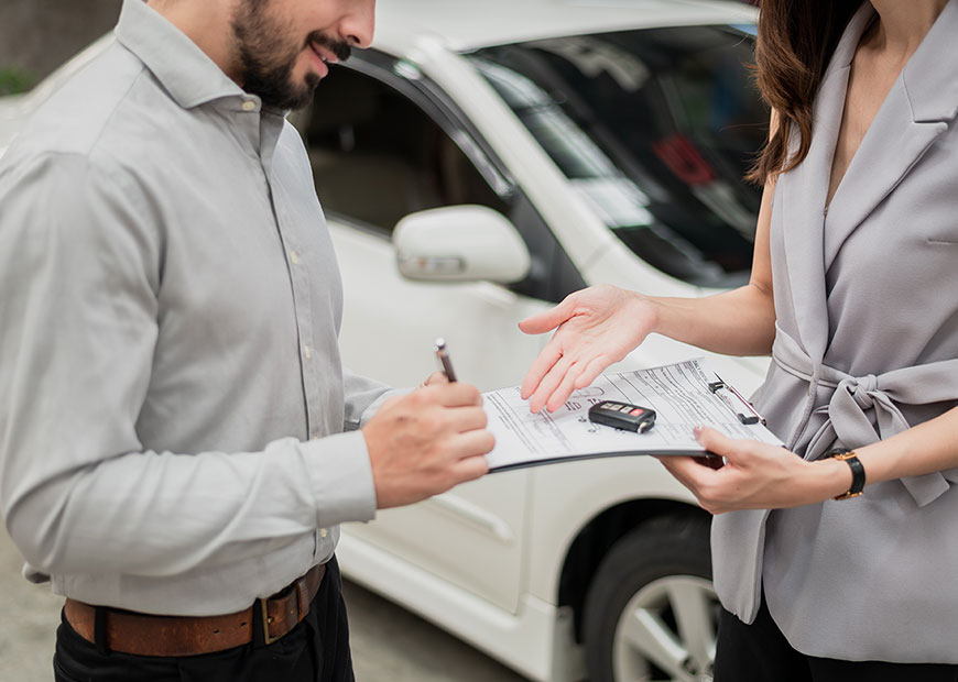 Image of man signing a paper with car in background